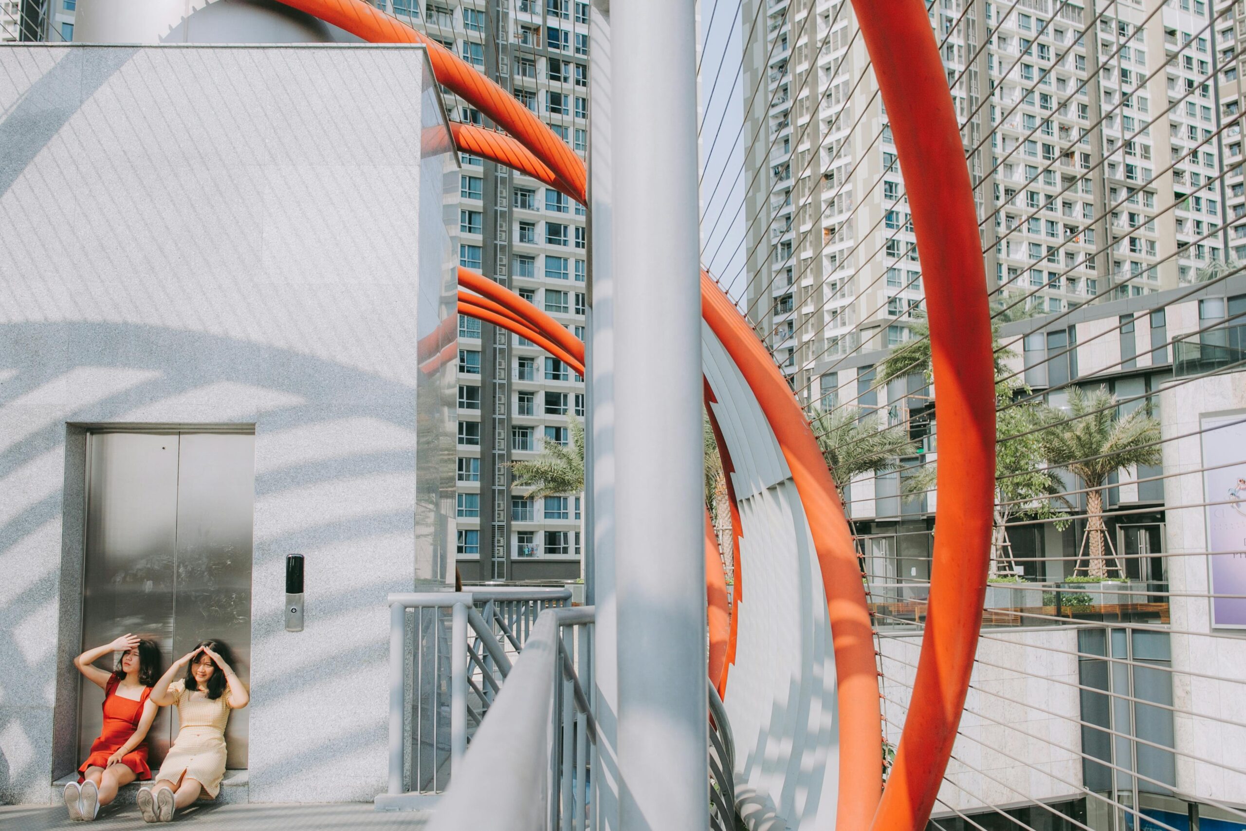 Urban scene with two women relaxing near an elevator amid striking architecture.